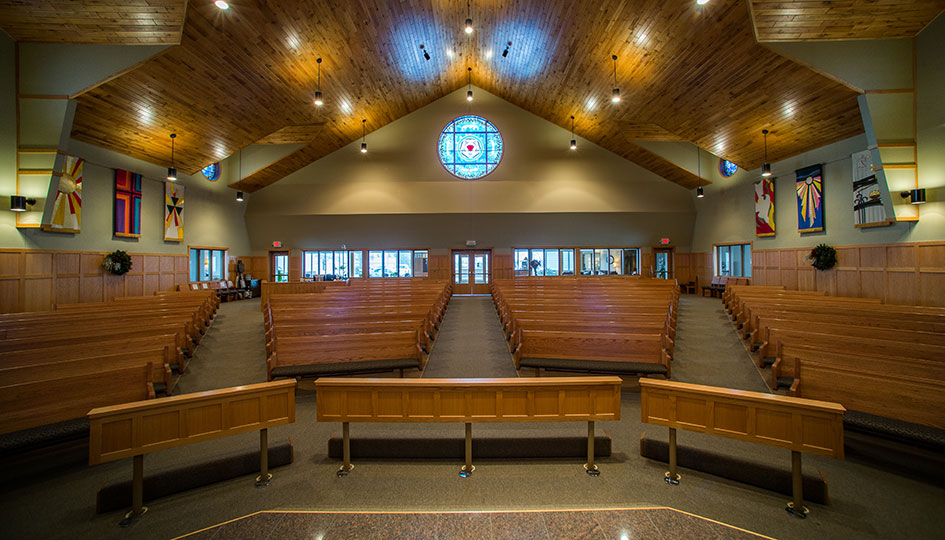 American Lutheran Church sanctuary with wood pews, vaulted ceiling, and stained glass window