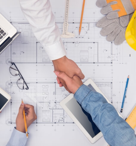 Construction professionals shaking hands over architectural blueprints