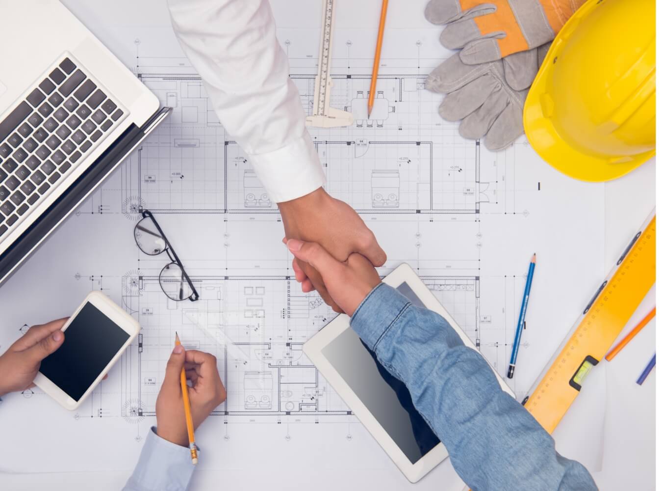 Construction team shaking hands over building plans and jobsite materials