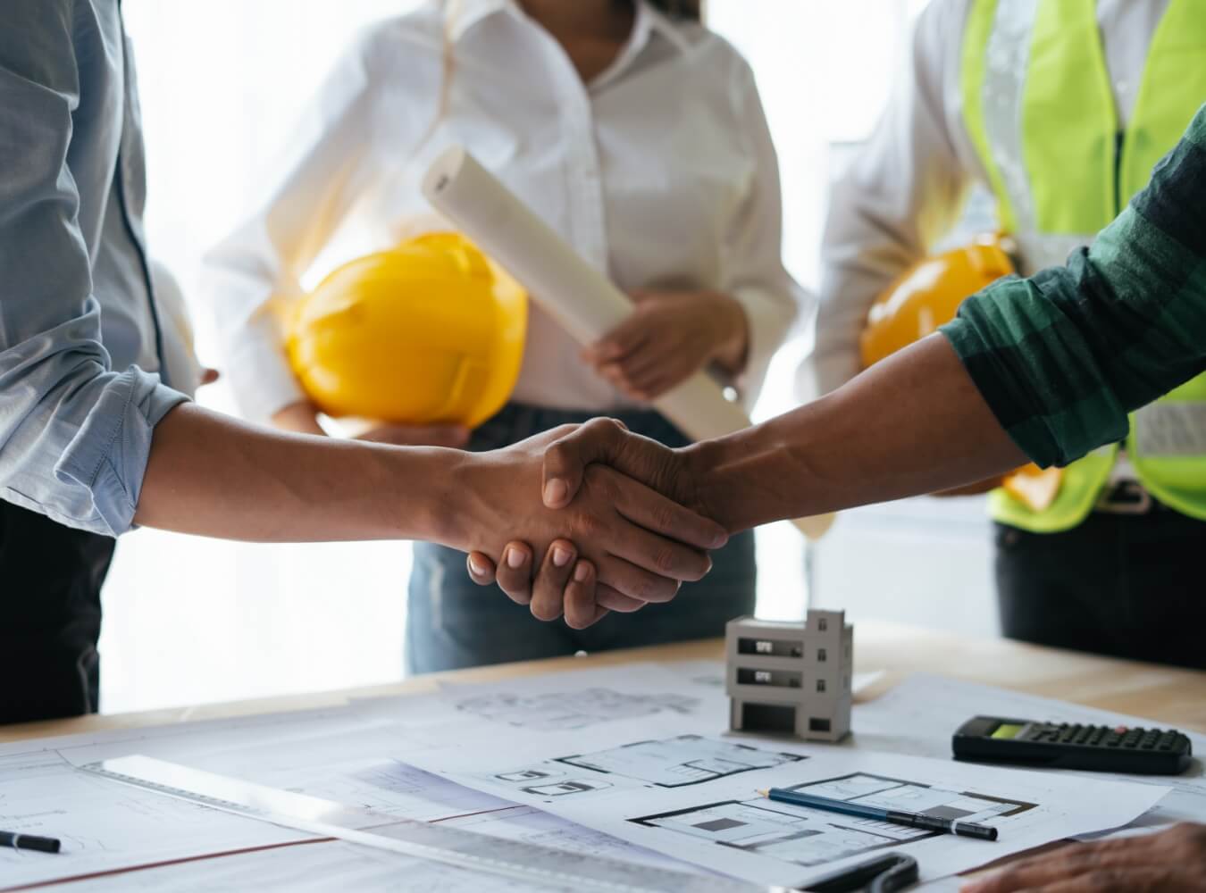 Construction team shaking hands over building plans during a project meeting