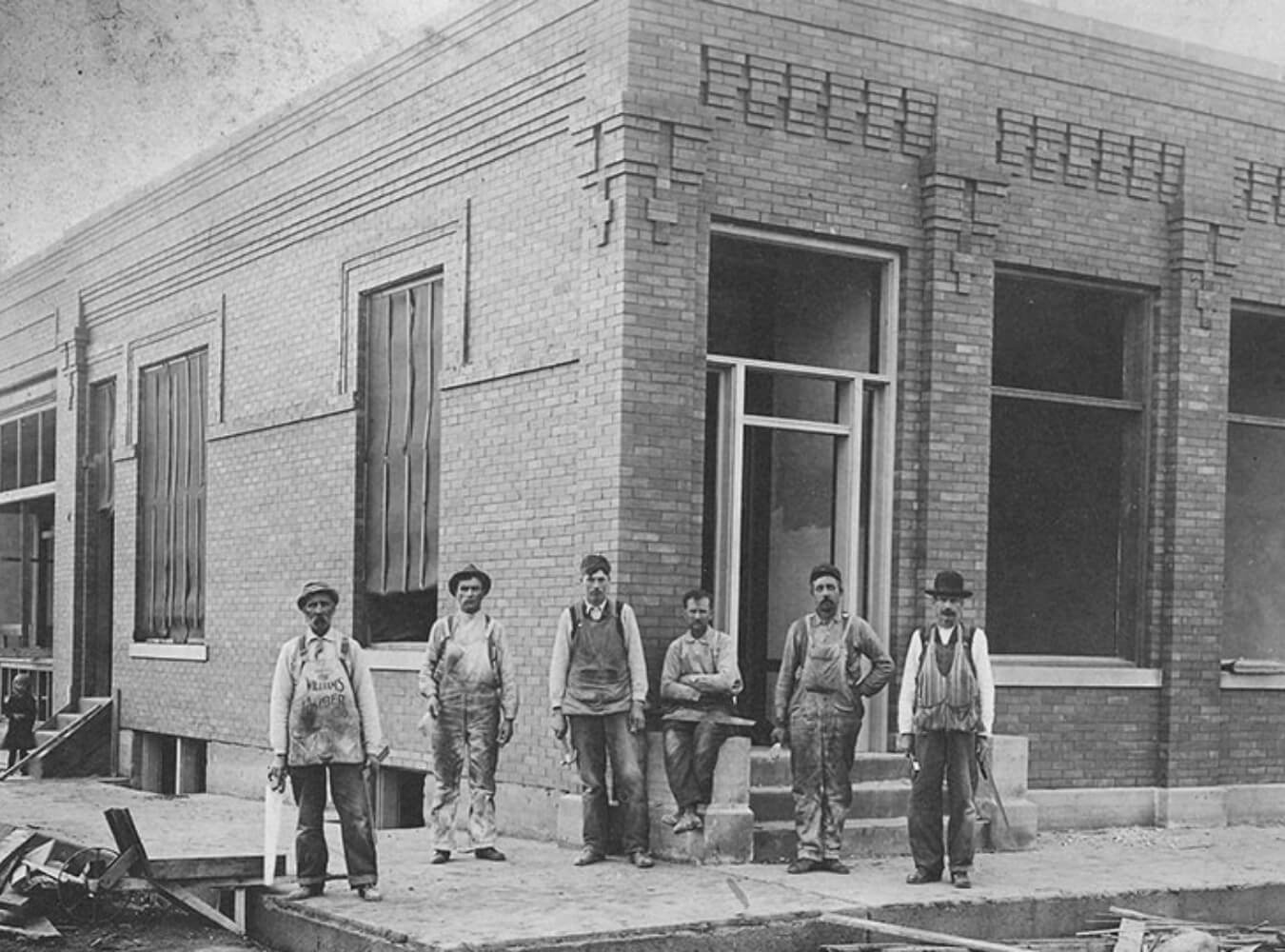 Historic construction crew standing outside a brick building under construction
